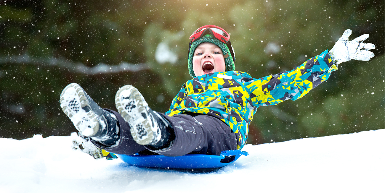 Young boy laughing as he Sleds down Sledding Hill