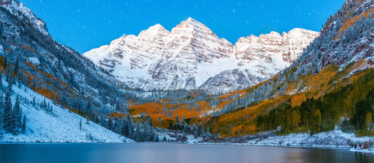 Maroon Bells in covered in snow during late fall with visitors on the bank