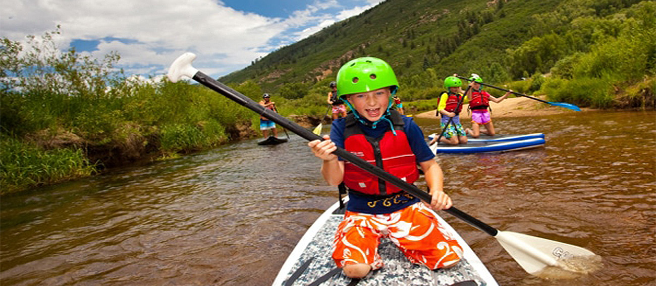 Young group of kids riding paddleboard going down Stillwater Stream in Aspen
