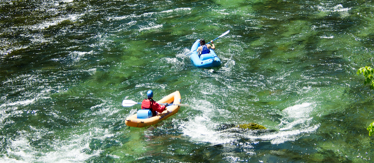 Two men going down calm stream in inflatable rafts