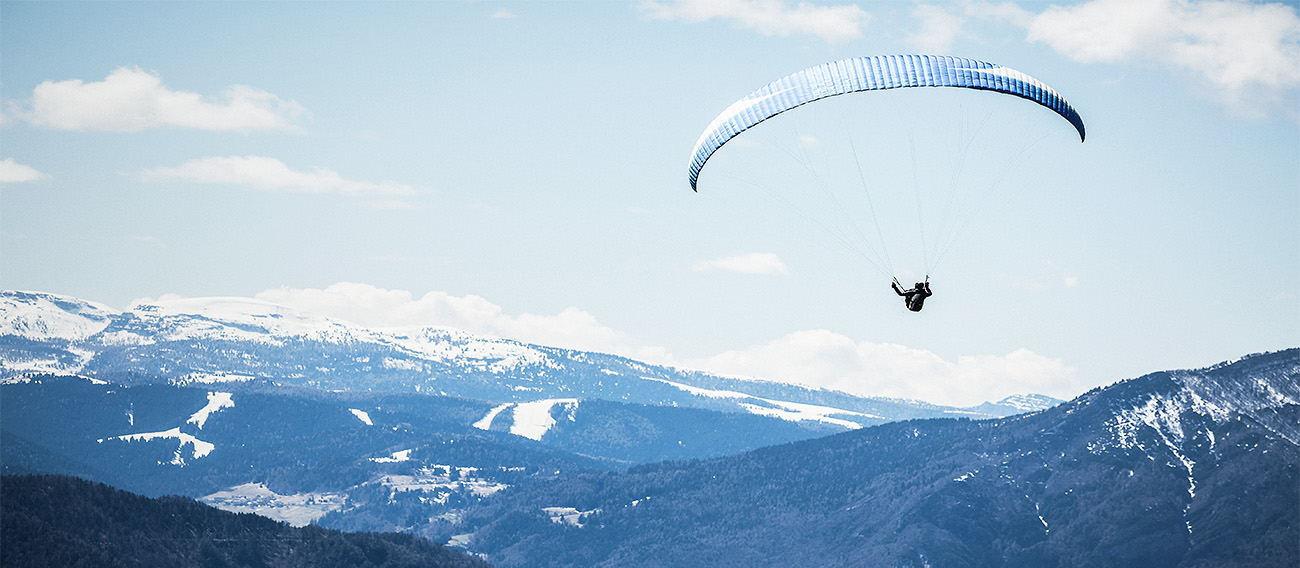 Man Paragliding through the air above mountains