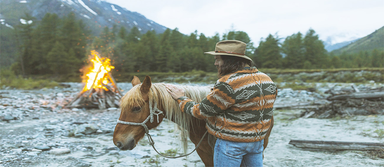 Man by campfire on lakeside with horse