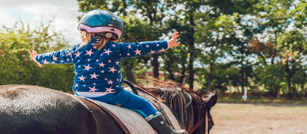 Small child on horseback riding with safety gear 