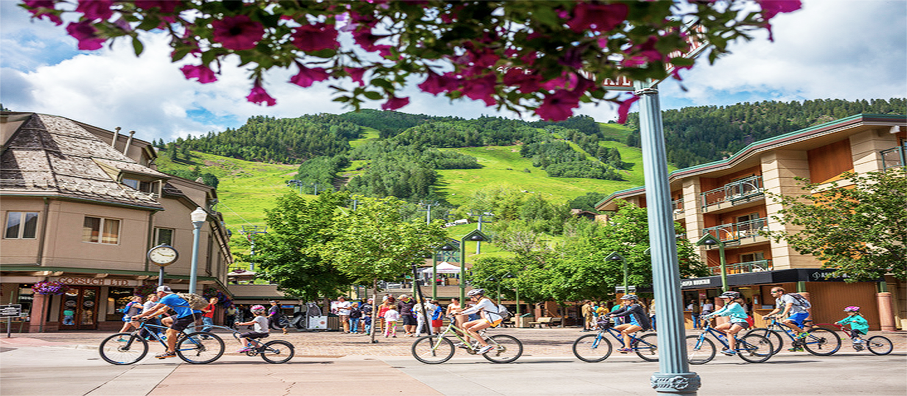 Family riding bikes on Aspen streets next to Aspen Mountain plaza in Aspen, Colorado during summer